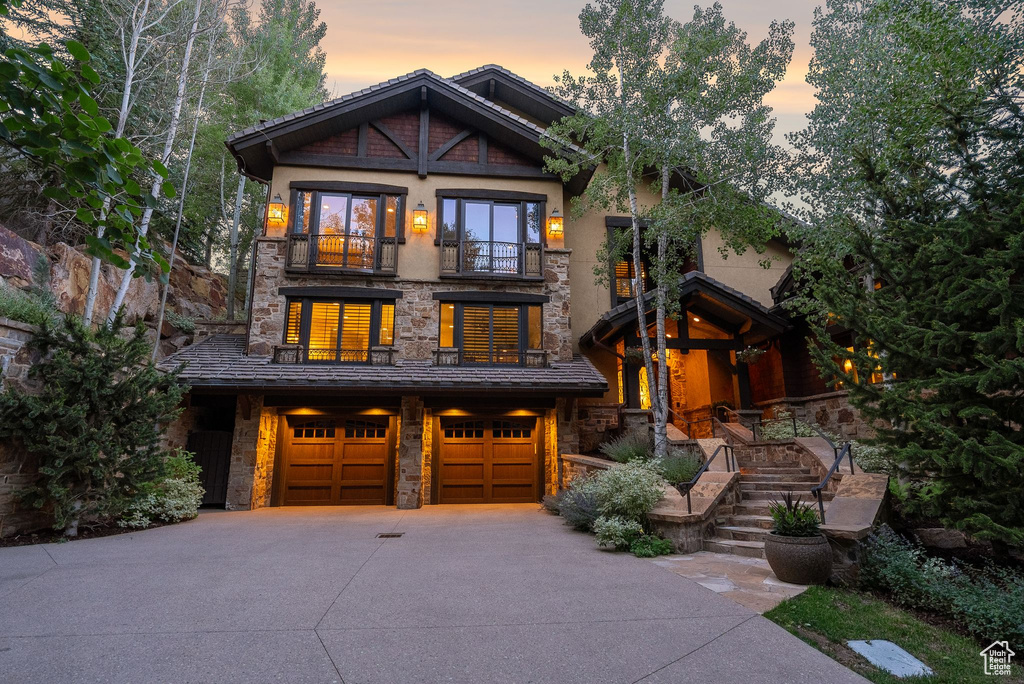 Craftsman house featuring a balcony, stone siding, a garage, concrete driveway, and stucco siding