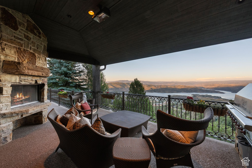 Balcony at dusk with an outdoor stone fireplace and a water and mountain view