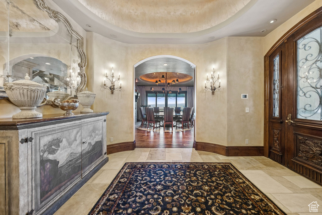 Foyer entrance with arched walkways, a chandelier, and a tray ceiling