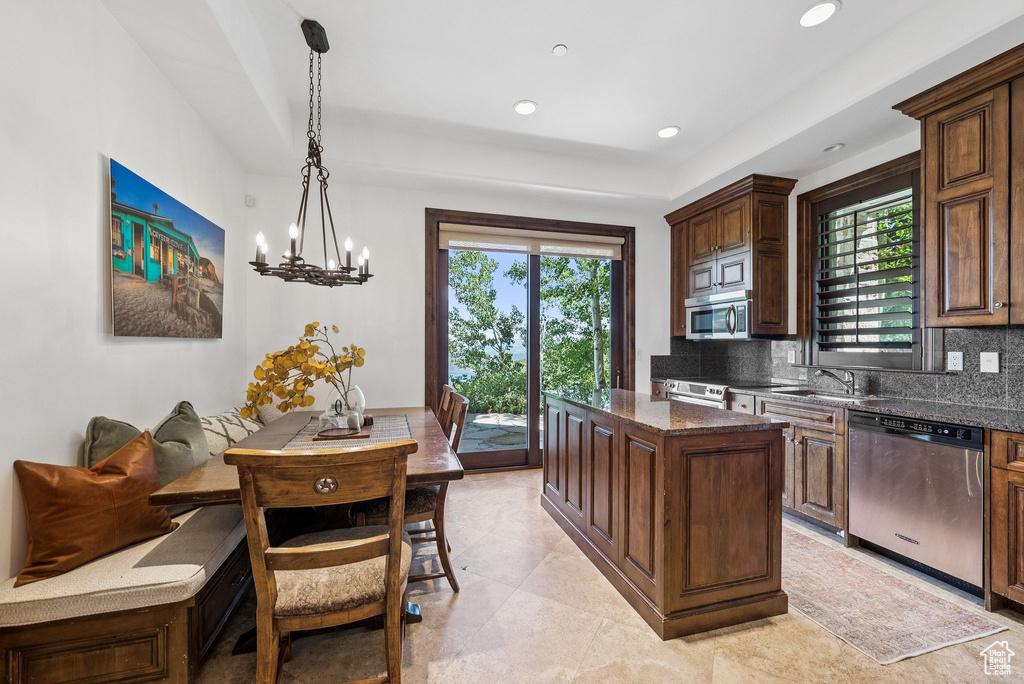 Kitchen featuring appliances with stainless steel finishes, tasteful backsplash, a center island, hanging light fixtures, and dark stone counters