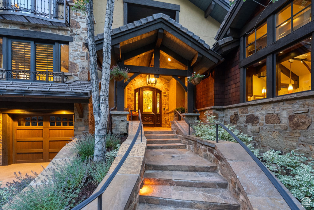 View of exterior entry with stone siding, a balcony, an attached garage, and stucco siding
