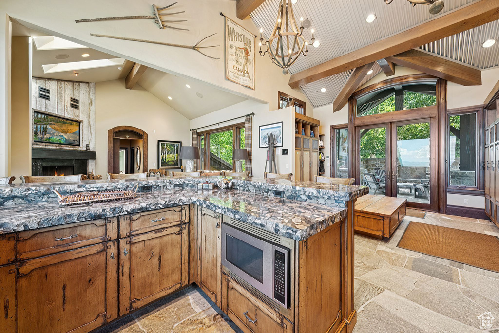 Kitchen featuring stone tile floors, stainless steel microwave, beam ceiling, a fireplace, and open floor plan