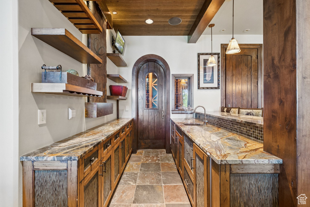 Bar featuring stone finish flooring, a wood ceiling with exposed beams, hanging light fixtures, arched walkways, and decorative backsplash