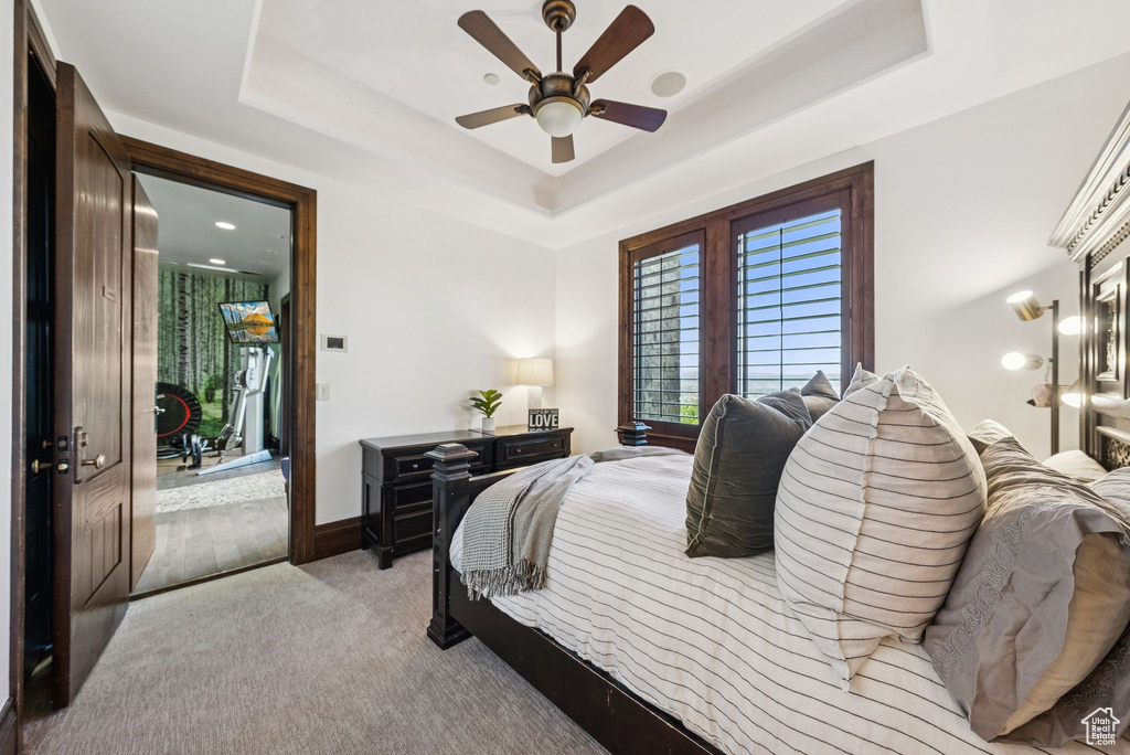 Bedroom featuring a tray ceiling, light colored carpet, and a ceiling fan