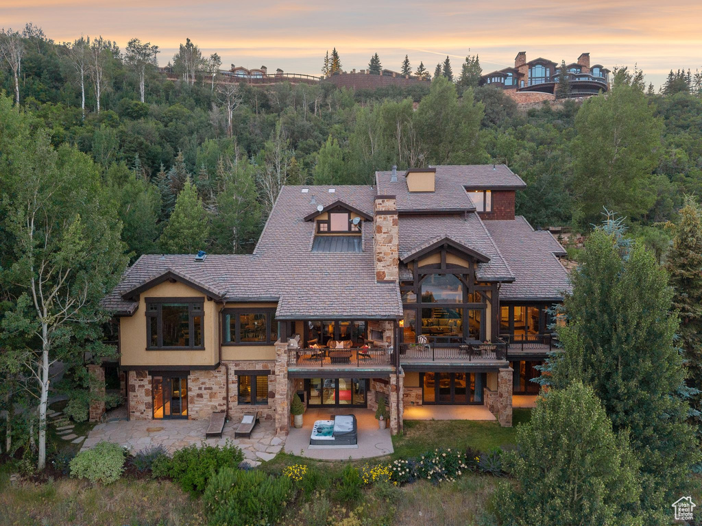 Rear view of property with a balcony, stone siding, a patio area, an outdoor hot tub, and french doors