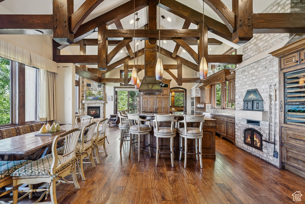 Dining room featuring a large fireplace, high vaulted ceiling, dark wood finished floors, and beam ceiling
