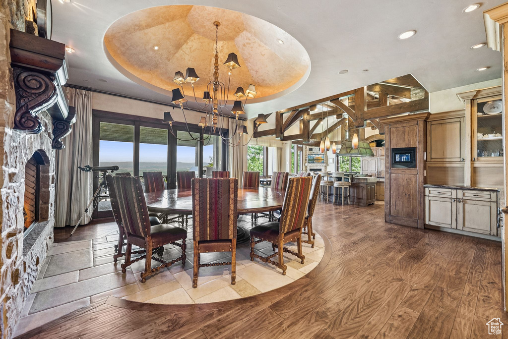 Dining room with a chandelier, a raised ceiling, dark wood finished floors, recessed lighting, and a fireplace