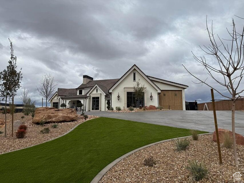 View of front of property with a front yard, a chimney, and concrete driveway