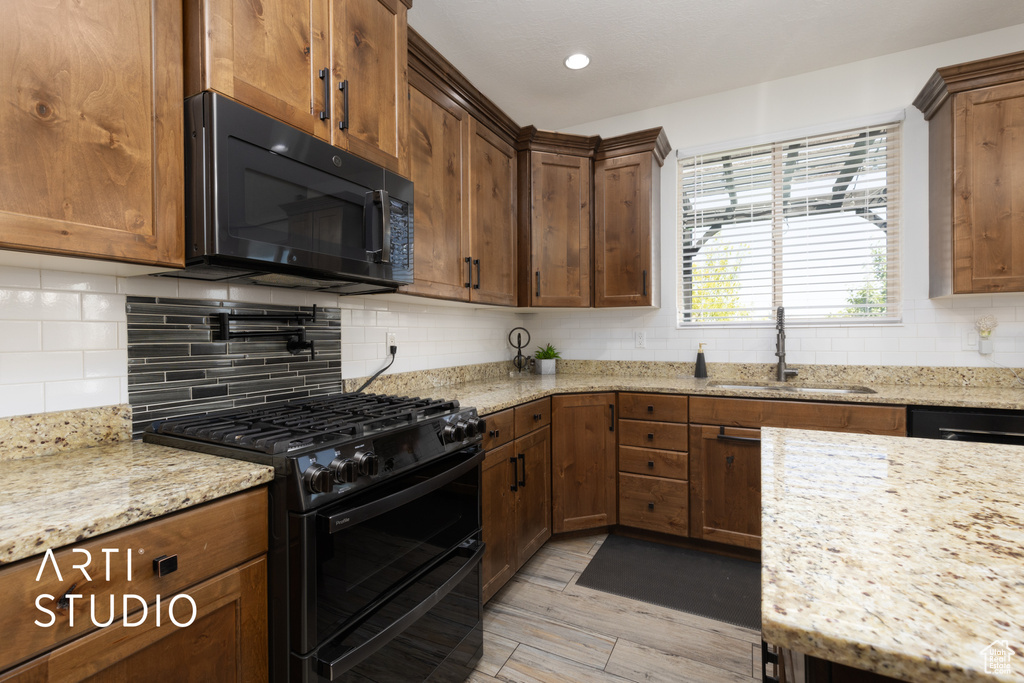 Kitchen with black appliances, backsplash, light stone counters, light wood-style flooring, and recessed lighting