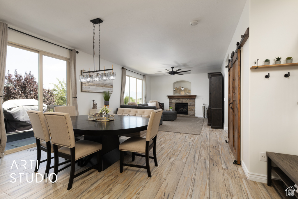 Dining space featuring a ceiling fan, light wood-style flooring, a stone fireplace, and a barn door