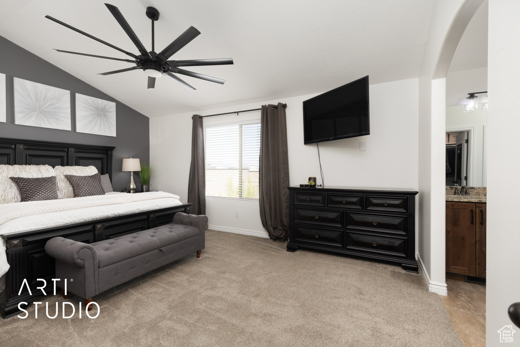 Bedroom featuring arched walkways, vaulted ceiling, light carpet, ensuite bath, and ceiling fan