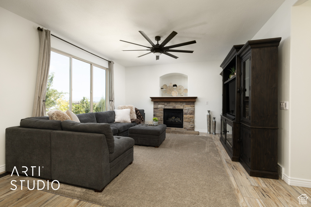 Living area with a ceiling fan, a stone fireplace, and light wood-style floors