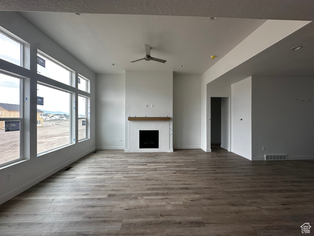 Unfurnished living room featuring ceiling fan, wood finished floors, and a fireplace