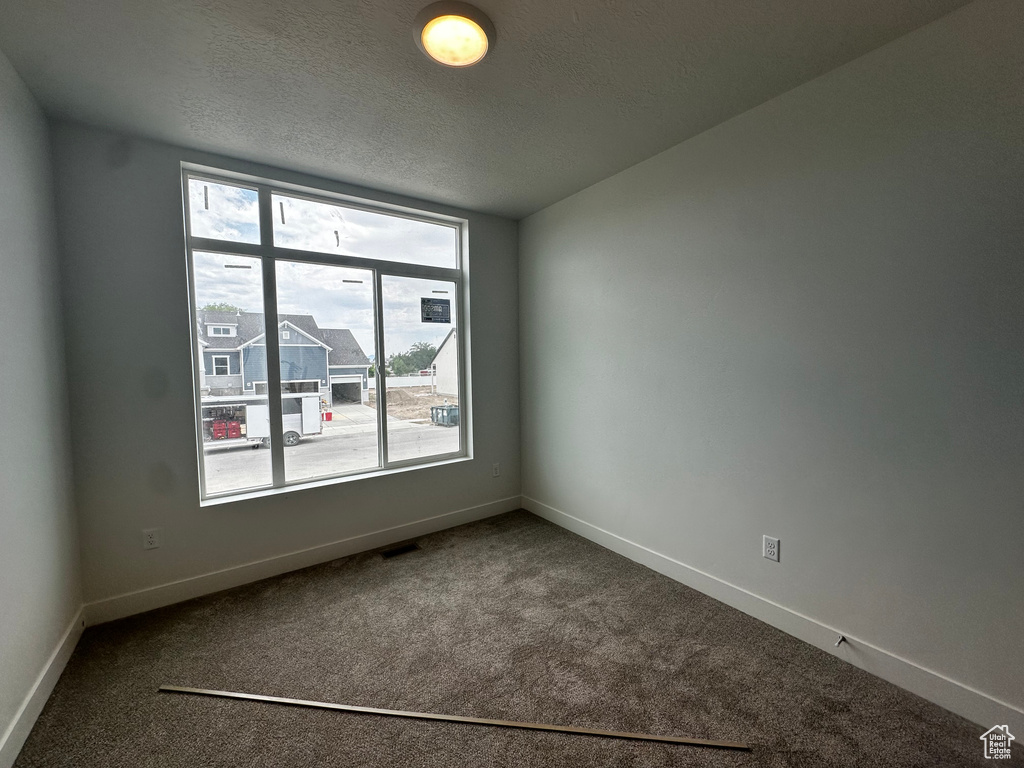Carpeted spare room featuring a textured ceiling and baseboards