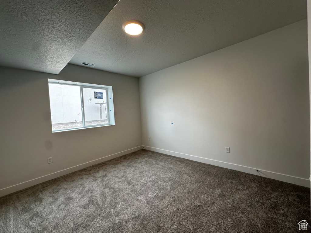 Unfurnished room with dark carpet and a textured ceiling