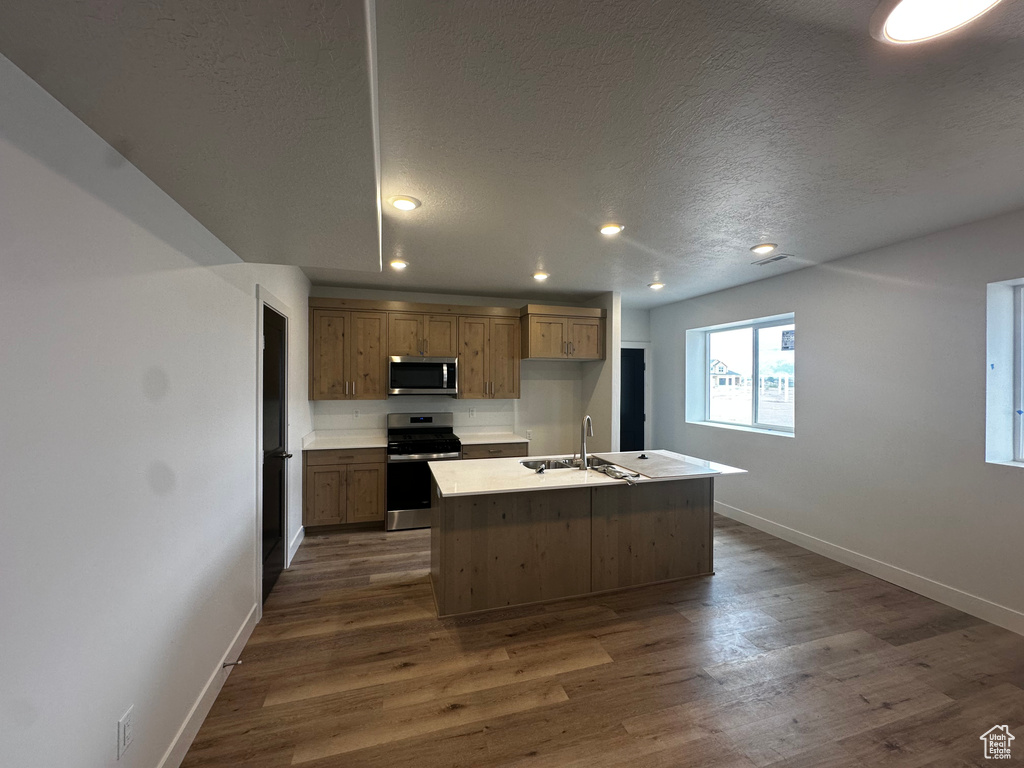 Kitchen with appliances with stainless steel finishes, an island with sink, dark wood-style floors, recessed lighting, and a textured ceiling