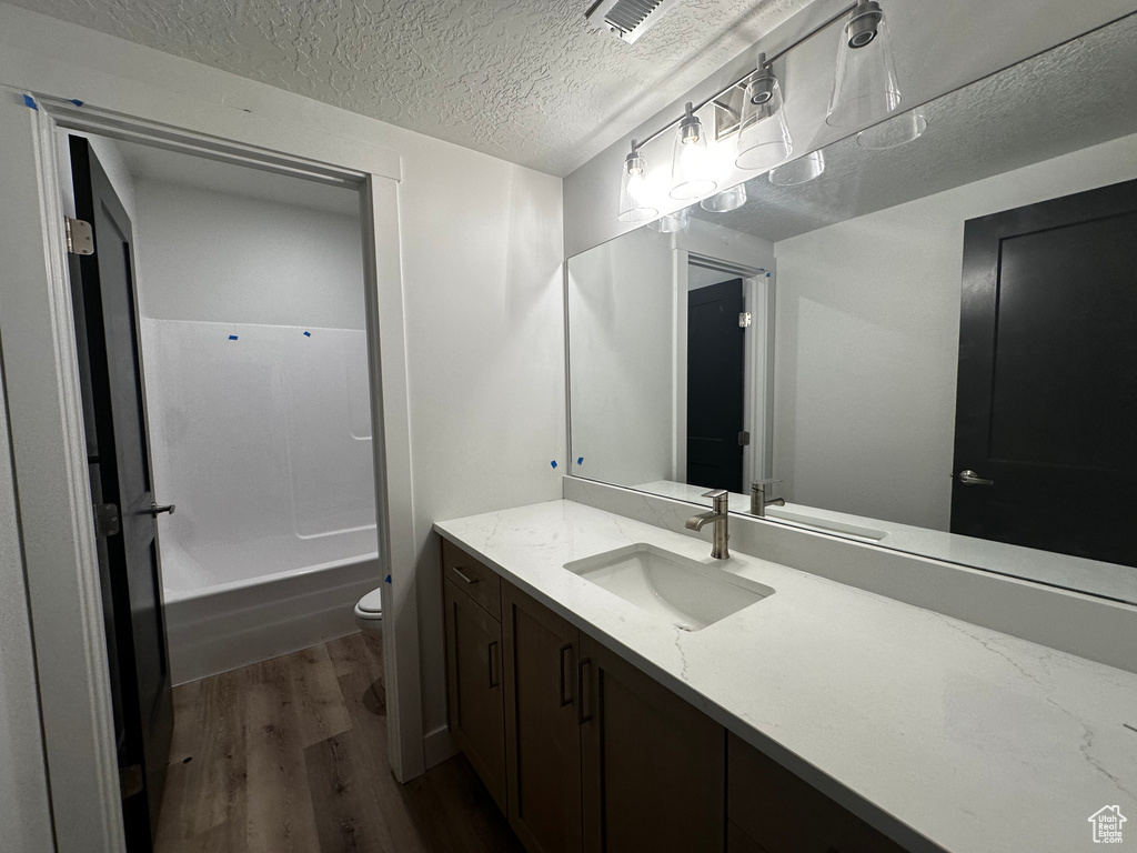 Full bathroom featuring wood finished floors, vanity, bathtub / shower combination, and a textured ceiling