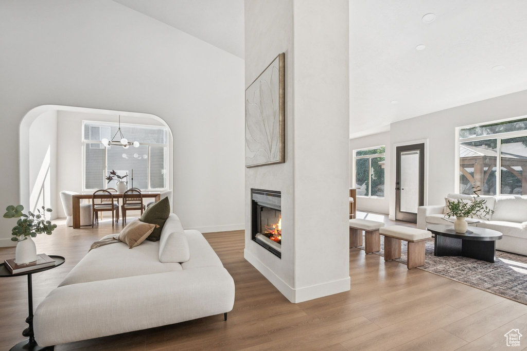 Living area featuring high vaulted ceiling, wood finished floors, a glass covered fireplace, and a chandelier