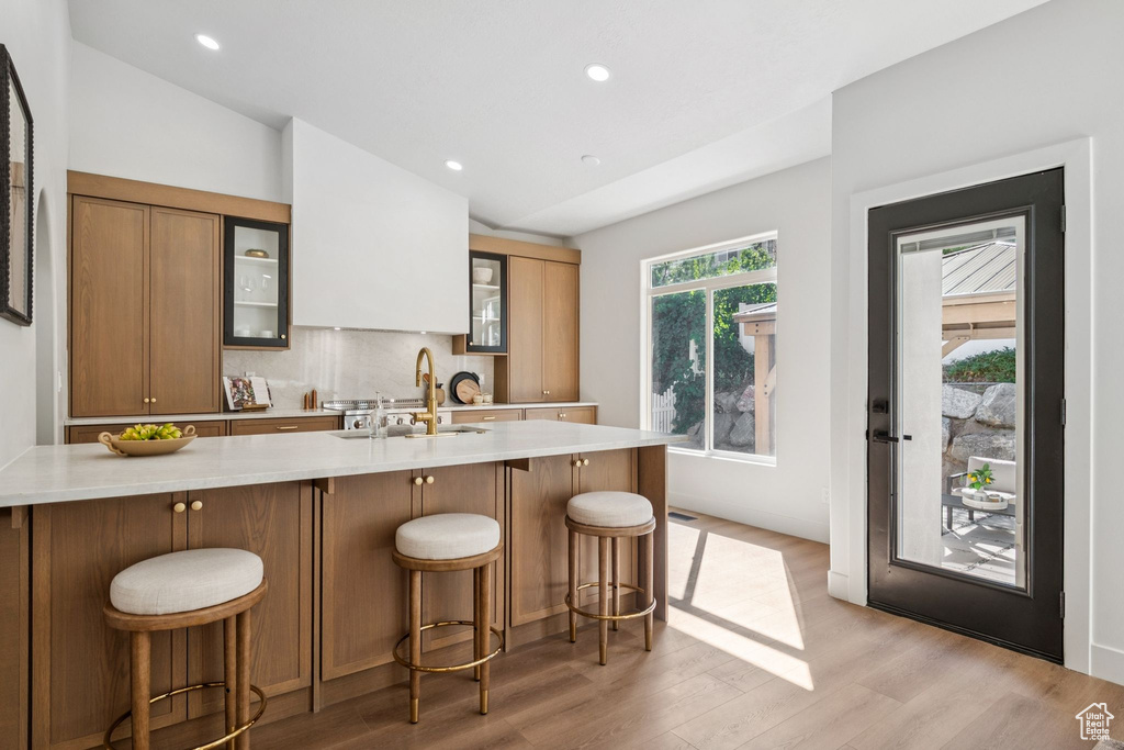 Kitchen featuring light countertops, light wood-style flooring, glass insert cabinets, lofted ceiling, and a breakfast bar