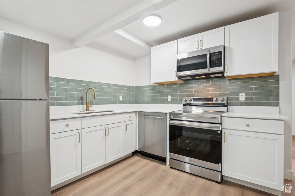 Kitchen featuring stainless steel appliances, light countertops, white cabinets, light wood finished floors, and tasteful backsplash