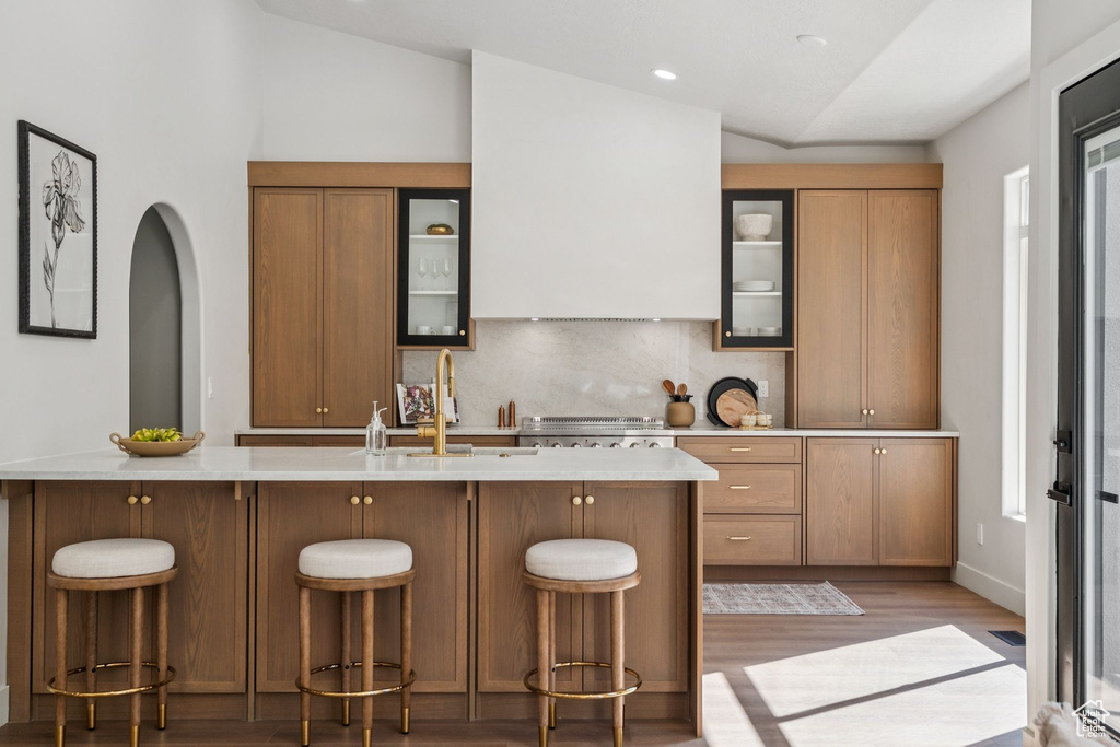 Kitchen featuring light wood finished floors, light countertops, lofted ceiling, backsplash, and glass insert cabinets