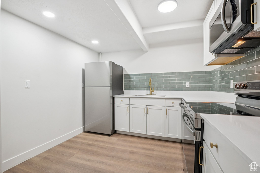 Kitchen with stainless steel appliances, white cabinetry, decorative backsplash, light countertops, and recessed lighting