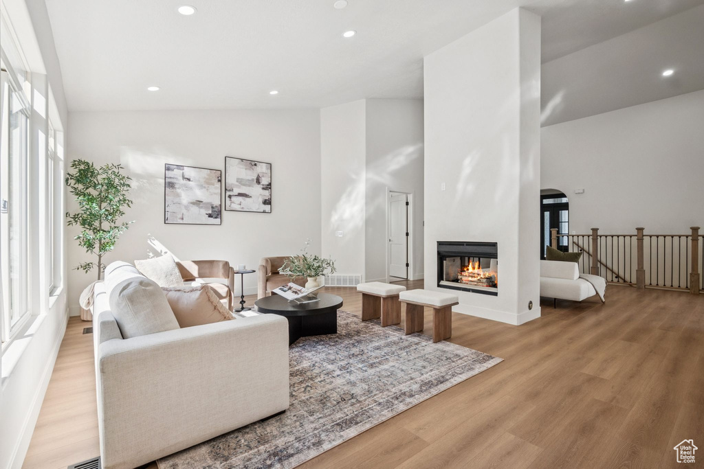 Living area with light wood-style floors, a multi sided fireplace, recessed lighting, arched walkways, and high vaulted ceiling