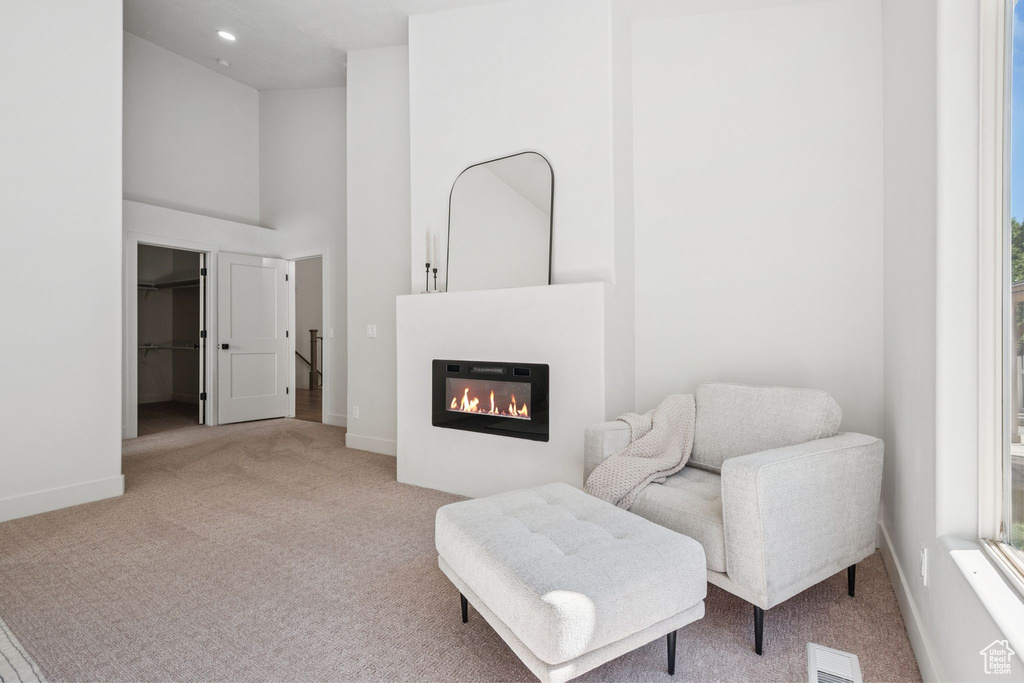 Sitting room with carpet flooring, a glass covered fireplace, a high ceiling, and recessed lighting