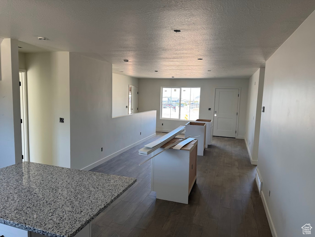 Kitchen with a kitchen island, dark wood-style flooring, a textured ceiling, and light stone countertops