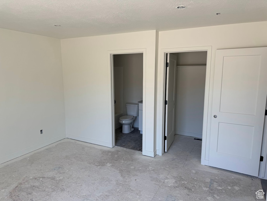 Unfurnished bedroom featuring a textured ceiling, ensuite bathroom, and a walk in closet