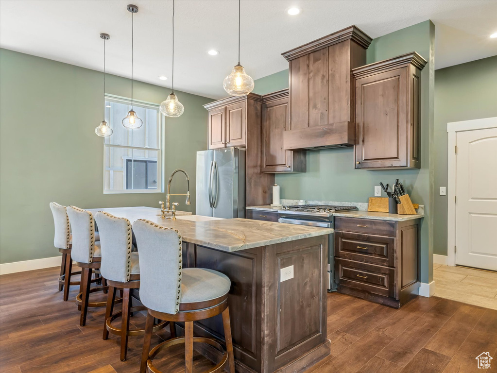 Kitchen with appliances with stainless steel finishes, dark wood-style flooring, a center island with sink, recessed lighting, and a kitchen bar