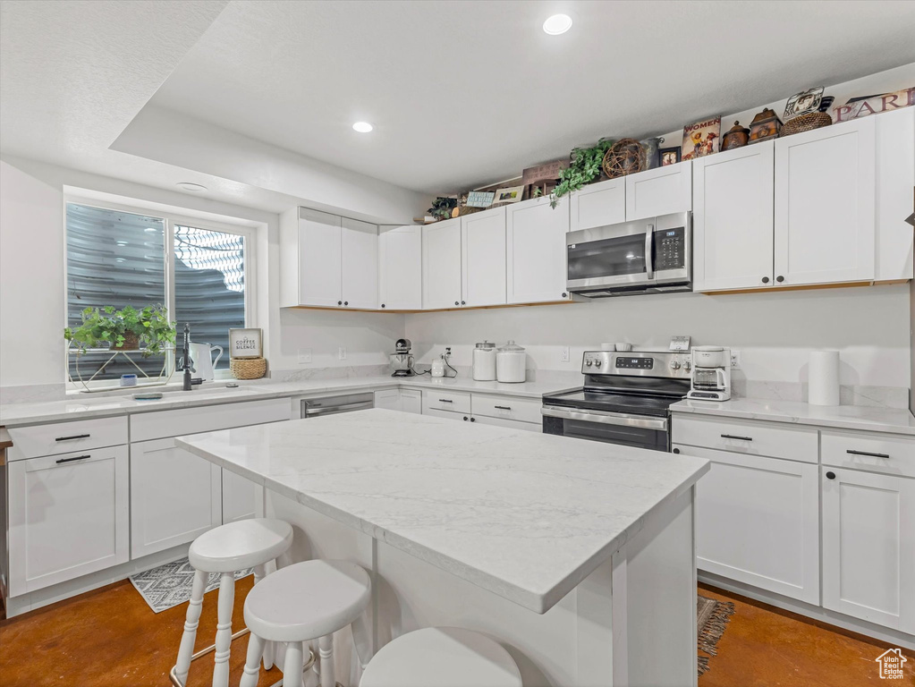 Kitchen featuring appliances with stainless steel finishes, a breakfast bar, recessed lighting, a center island, and white cabinetry