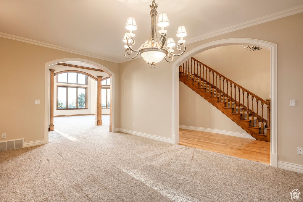 Empty room with arched walkways, carpet flooring, ornamental molding, stairs, and a chandelier