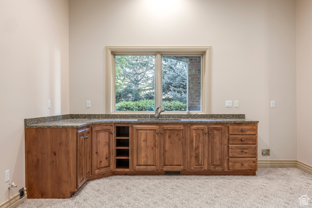 Kitchen with brown cabinets, light carpet, and dark stone countertops