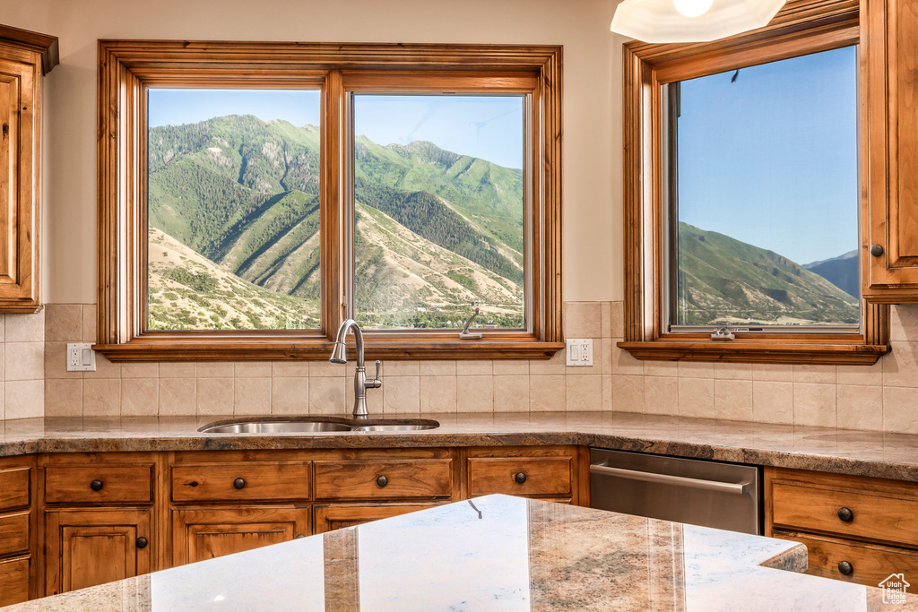 Kitchen with brown cabinetry, stainless steel dishwasher, a mountain view, backsplash, and stone countertops