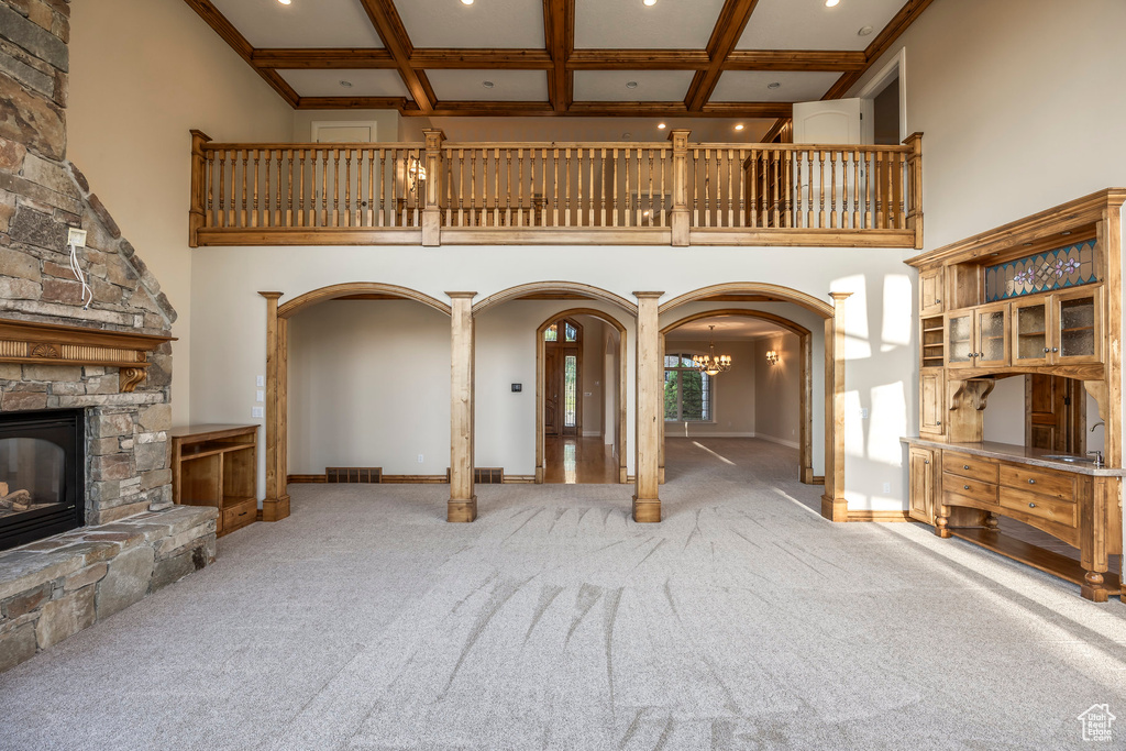 Unfurnished living room with arched walkways, a towering ceiling, carpet, a stone fireplace, and coffered ceiling