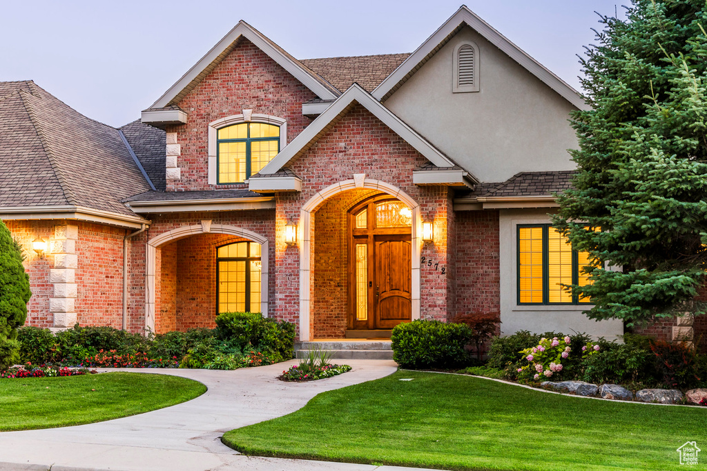 View of front facade featuring brick siding, a front yard, stucco siding, and roof with shingles