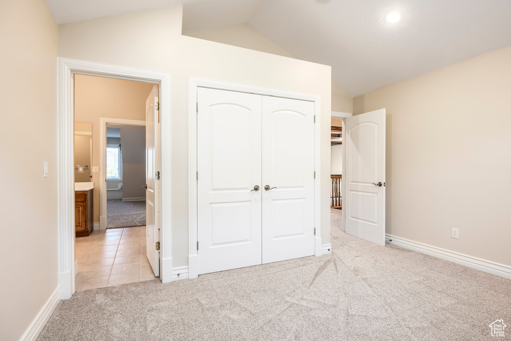 Unfurnished bedroom with light colored carpet, vaulted ceiling, a closet, and light tile patterned floors