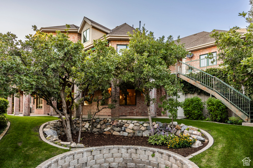 View of front of property with brick siding, a front yard, stairway, and stucco siding