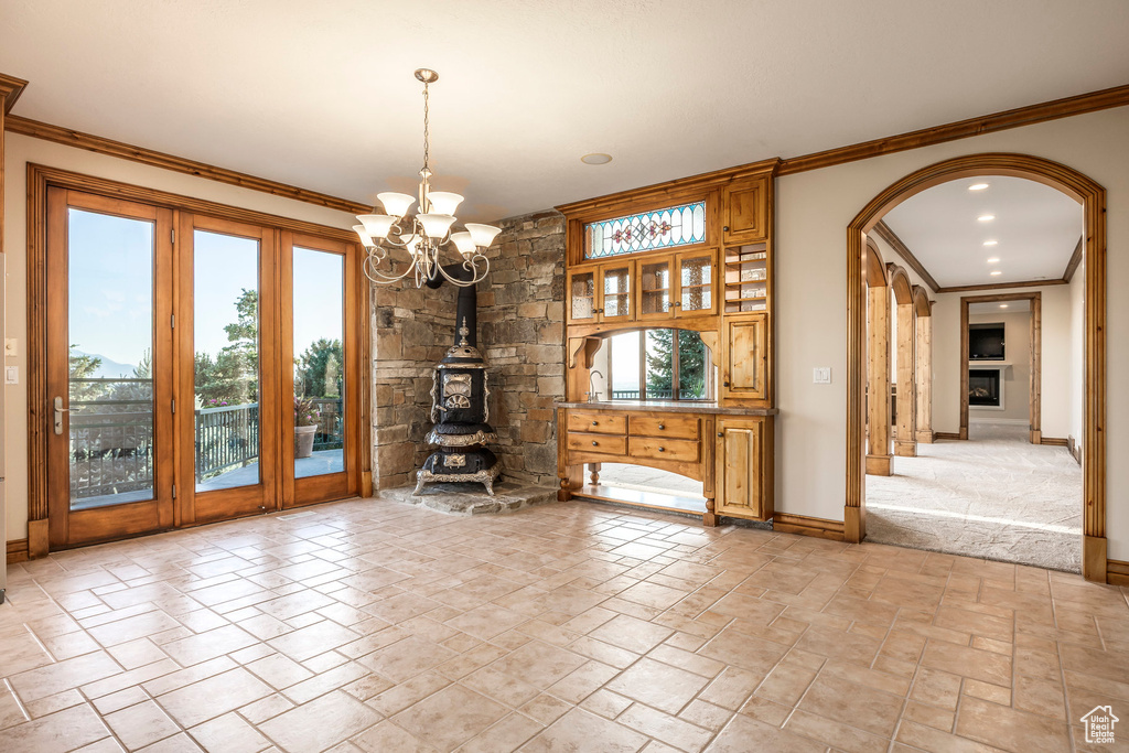 Unfurnished living room with arched walkways, a chandelier, stone tile floors, a wood stove, and ornamental molding
