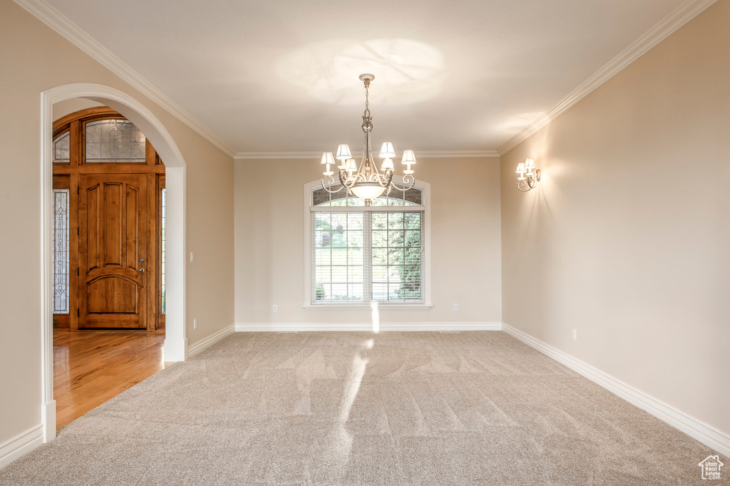 Unfurnished room with arched walkways, light carpet, a chandelier, and crown molding