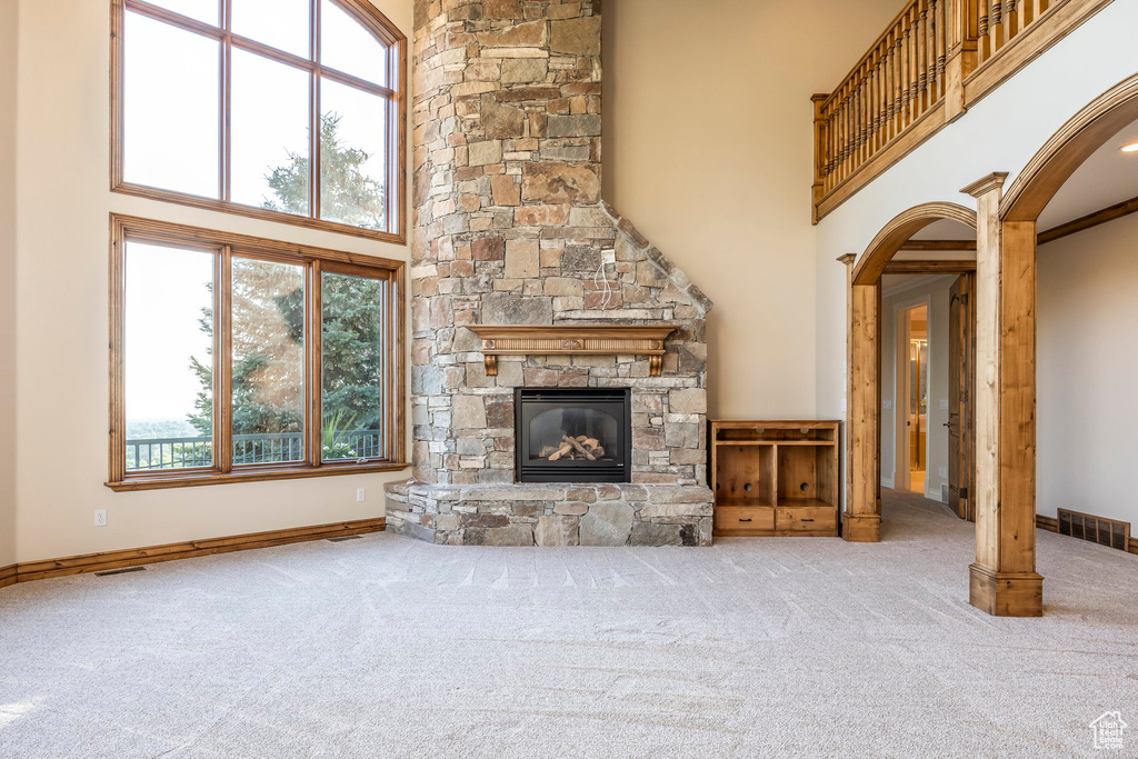 Unfurnished living room with carpet, arched walkways, a towering ceiling, a stone fireplace, and decorative columns