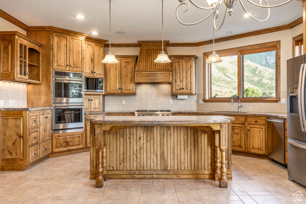 Kitchen featuring backsplash, appliances with stainless steel finishes, brown cabinetry, light stone counters, and ornamental molding