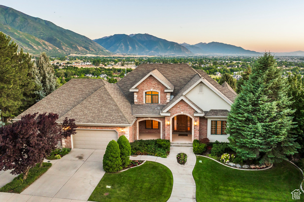 View of front of home with an attached garage, brick siding, driveway, a lawn, and a mountain view