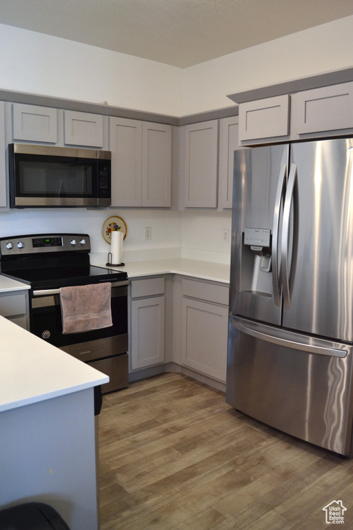 Kitchen featuring stainless steel appliances, gray cabinetry, light countertops, and light wood-type flooring