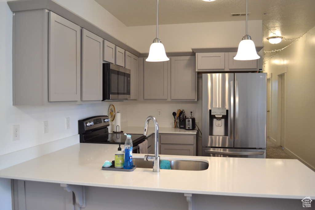 Kitchen featuring stainless steel appliances, gray cabinetry, a peninsula, and light countertops