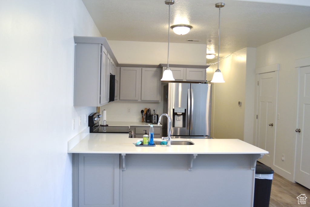 Kitchen featuring stainless steel fridge with ice dispenser, range with electric stovetop, gray cabinets, a peninsula, and a kitchen bar