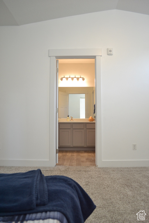 Bedroom featuring vaulted ceiling, ensuite bathroom, and carpet flooring