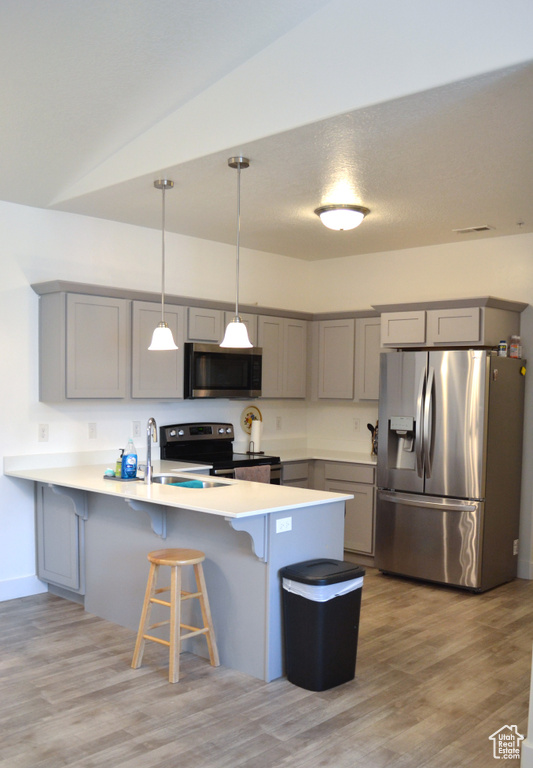 Kitchen featuring stainless steel appliances, gray cabinetry, a peninsula, a breakfast bar area, and lofted ceiling