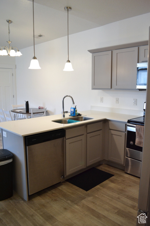 Kitchen with appliances with stainless steel finishes, gray cabinetry, a peninsula, and dark wood-style floors